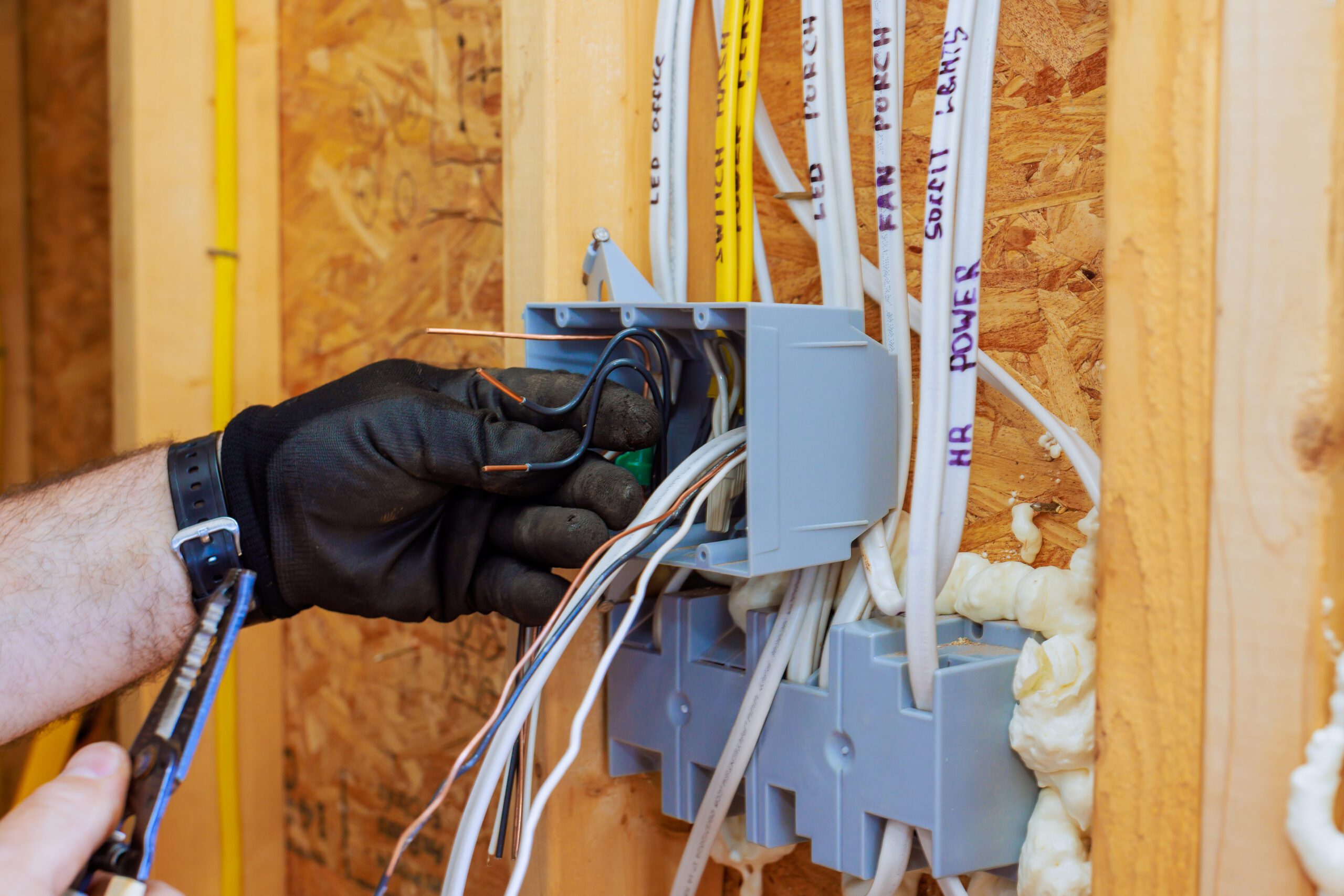 Electrician installing electrical wiring inside a residential wall during new construction.